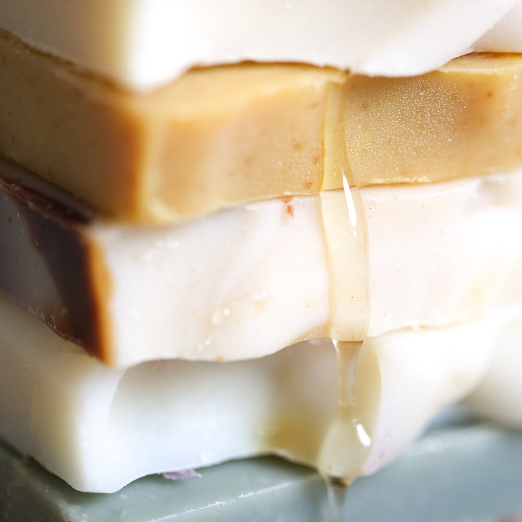 Stacked bars of handmade goat milk and tallow soap with honey dripping down the side.